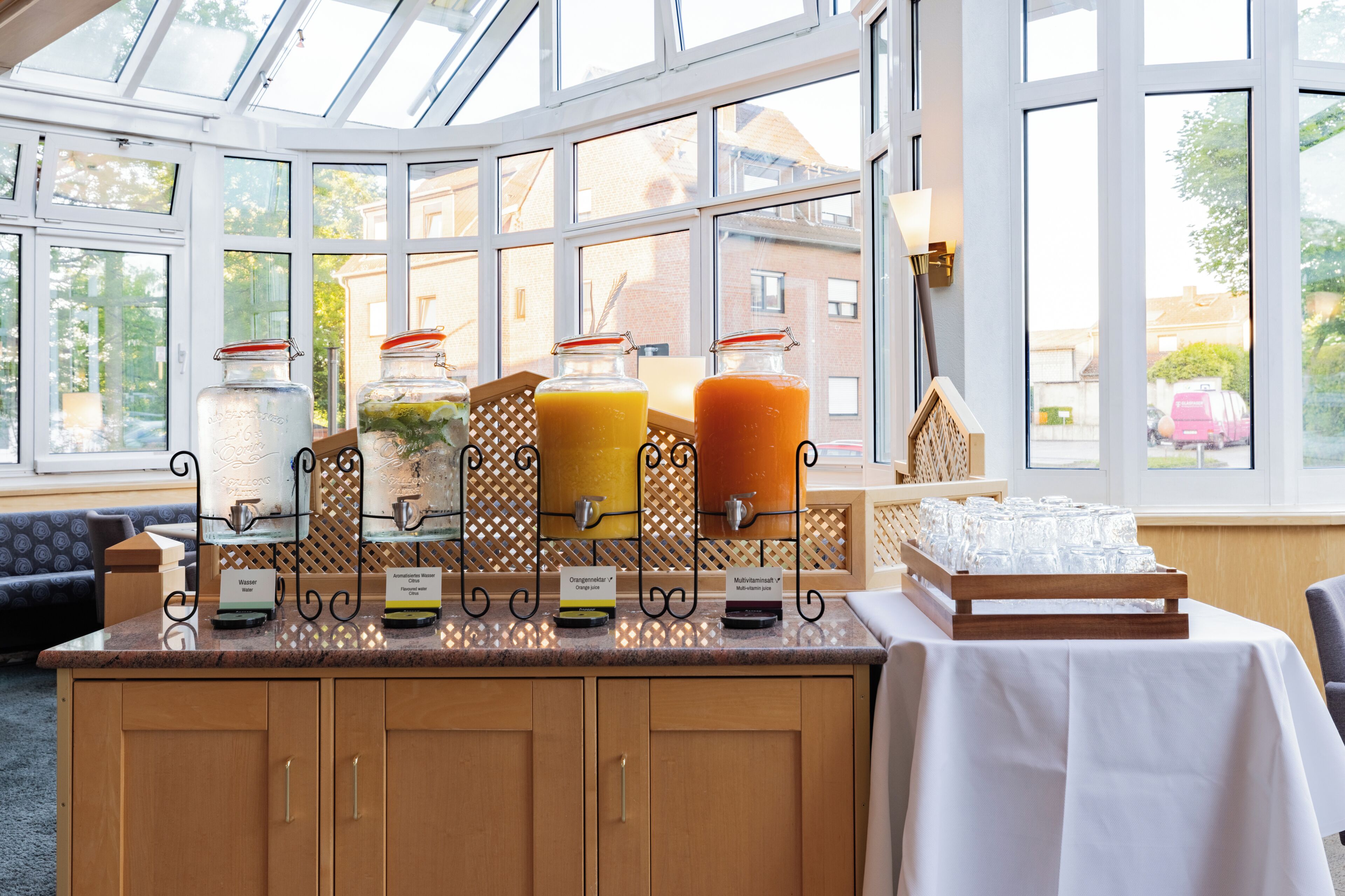 A breakfast bar with juice dispensers, a white tablecloth, and a view through large windows.