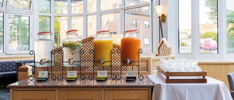 A breakfast bar with juice dispensers, a white tablecloth, and a view through large windows.