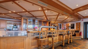 Zona de bar con taburetes de madera, una barra y una cocina al fondo.