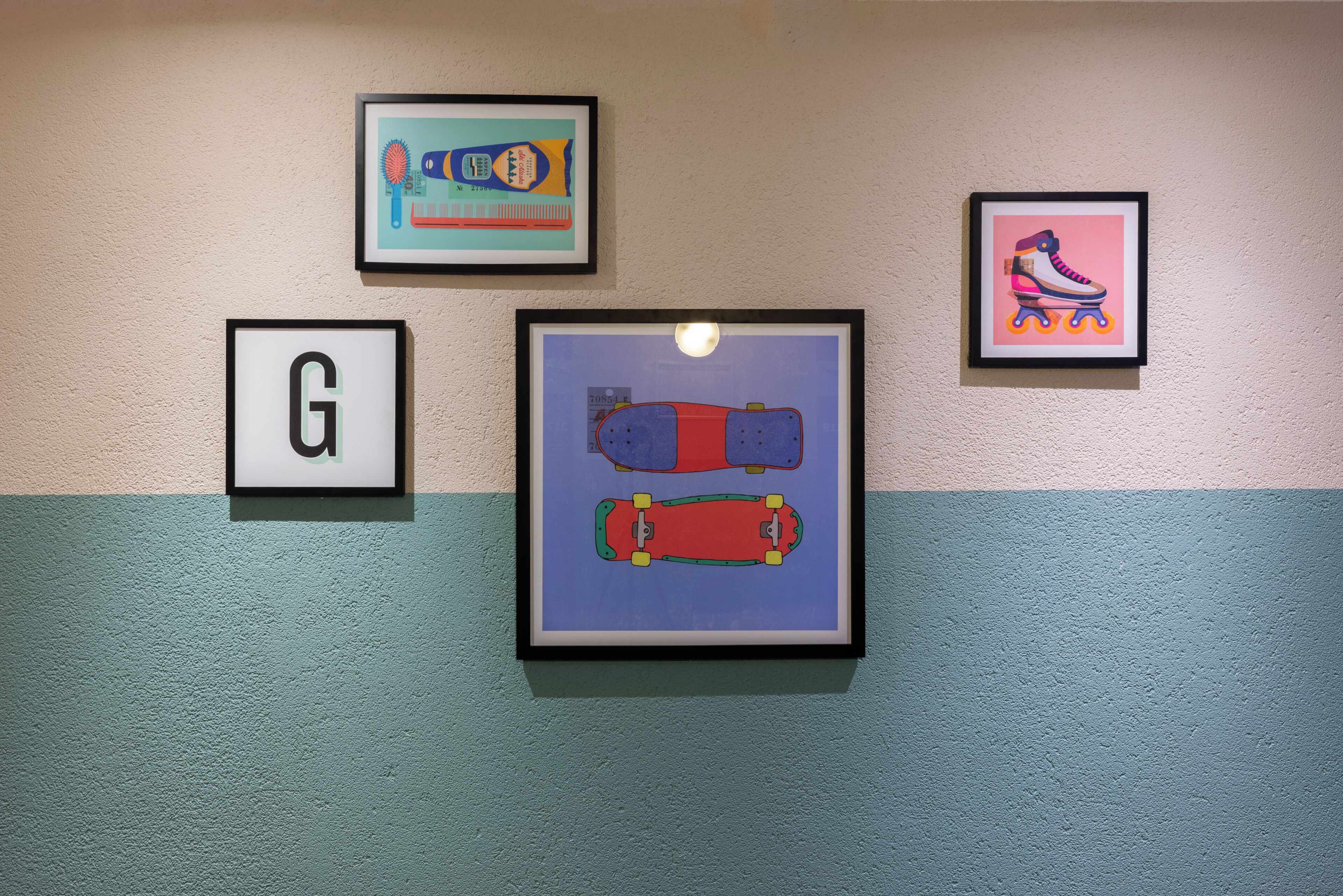 Eine Wand mit vier gerahmten Kunstwerken, darunter ein Skateboard und ein Buchstabe 'G'.