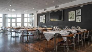 Un restaurante con varias mesas dispuestas para comer, con un interior moderno, piso de madera y una pared oscura decorada con impresiones botánicas enmarcadas.