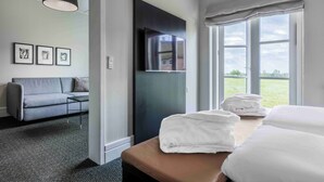 Habitación de hotel con sofá, televisor de pantalla plana, ventana grande con vistas y mesa de masaje con toallas.