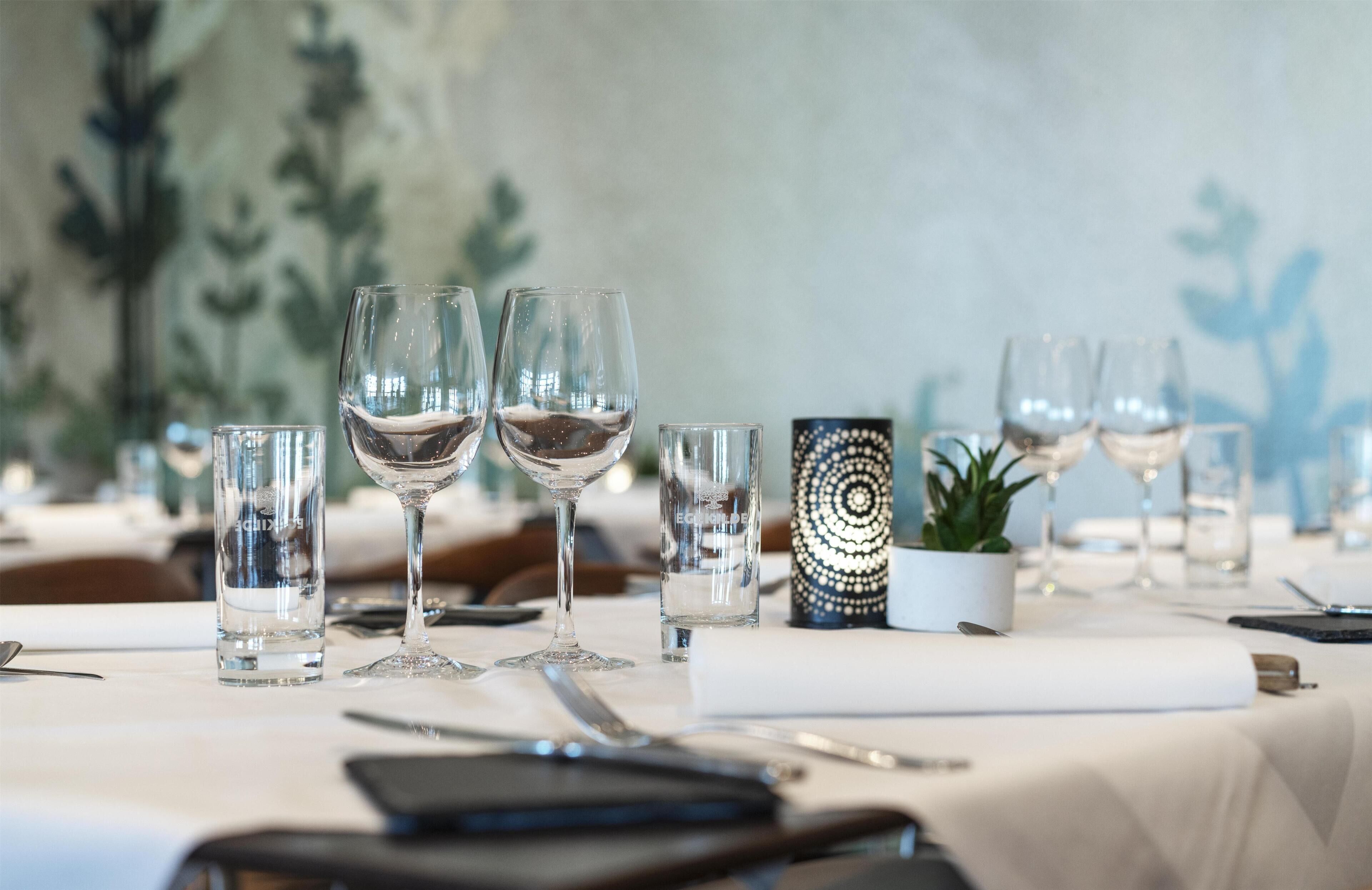 A dining table set with multiple wine glasses, a small potted plant, and a decorative item.