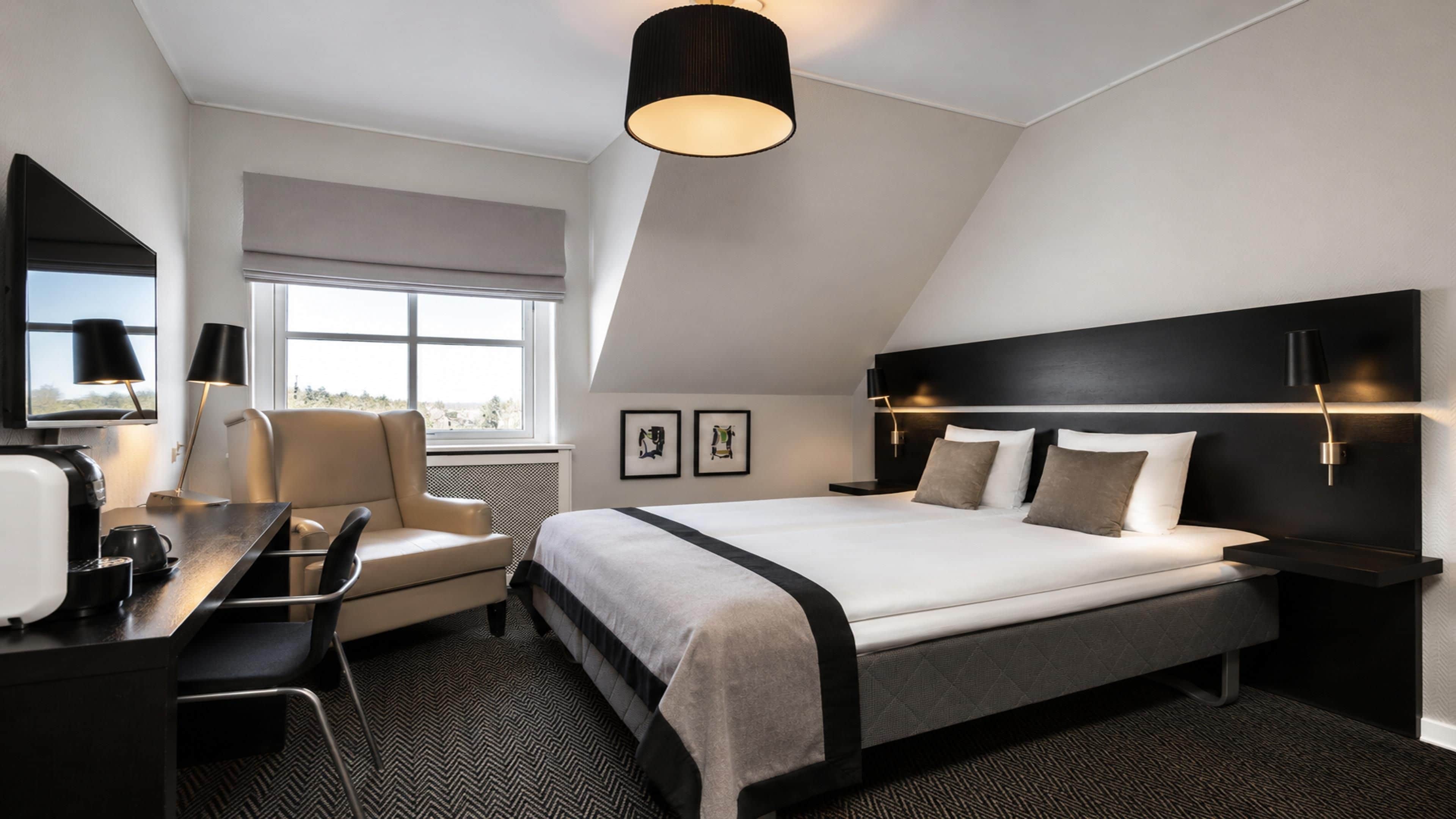 Une chambre d’hôtel moderne équipée d’un lit, d’un bureau, d’une chaise et d’une grande fenêtre.