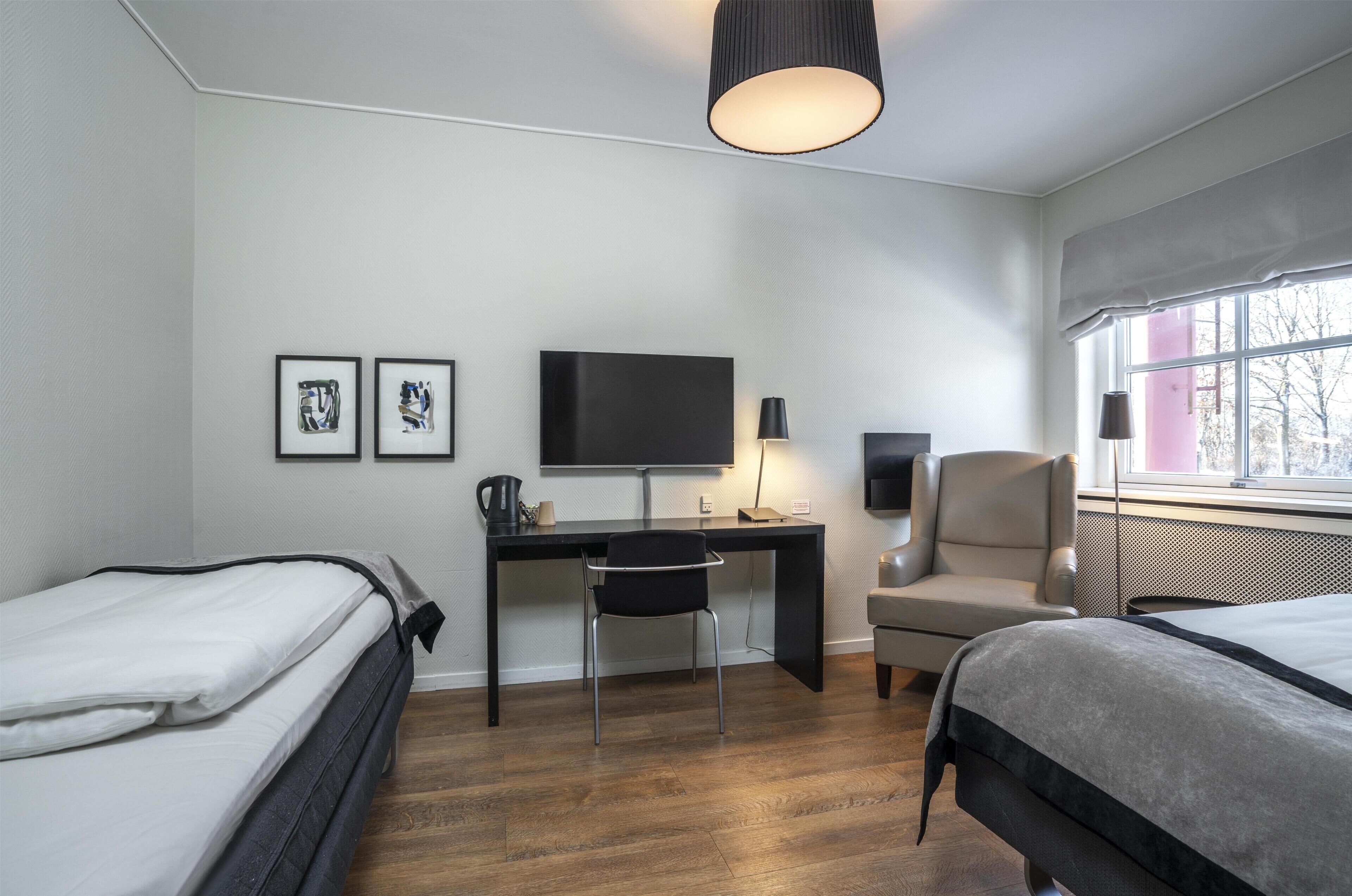 A hotel room with two beds, a desk with a chair, a television, and a window with a view.