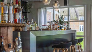 Zona de bar con mostrador de madera, taburetes y una variedad de botellas de licor.