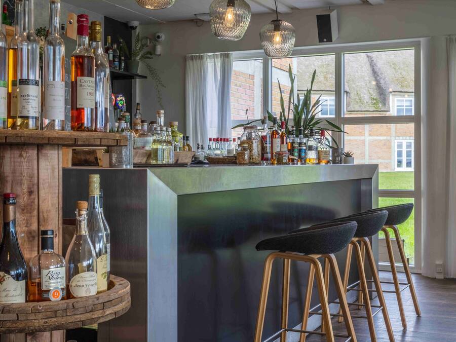 Zona de bar con mostrador de madera, taburetes y una variedad de botellas de licor.