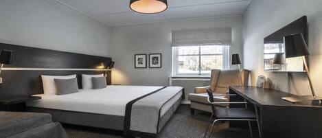 A hotel room with a bed, desk, chair, and a large window.