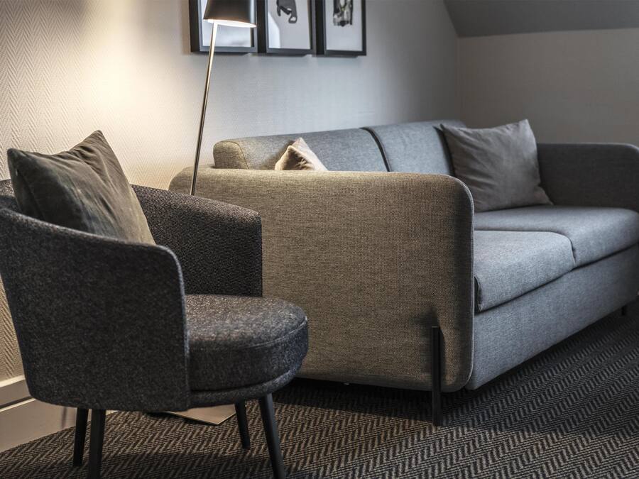 Una sala de estar moderna con un sofá gris, un sillón oscuro y una alfombra estampada.