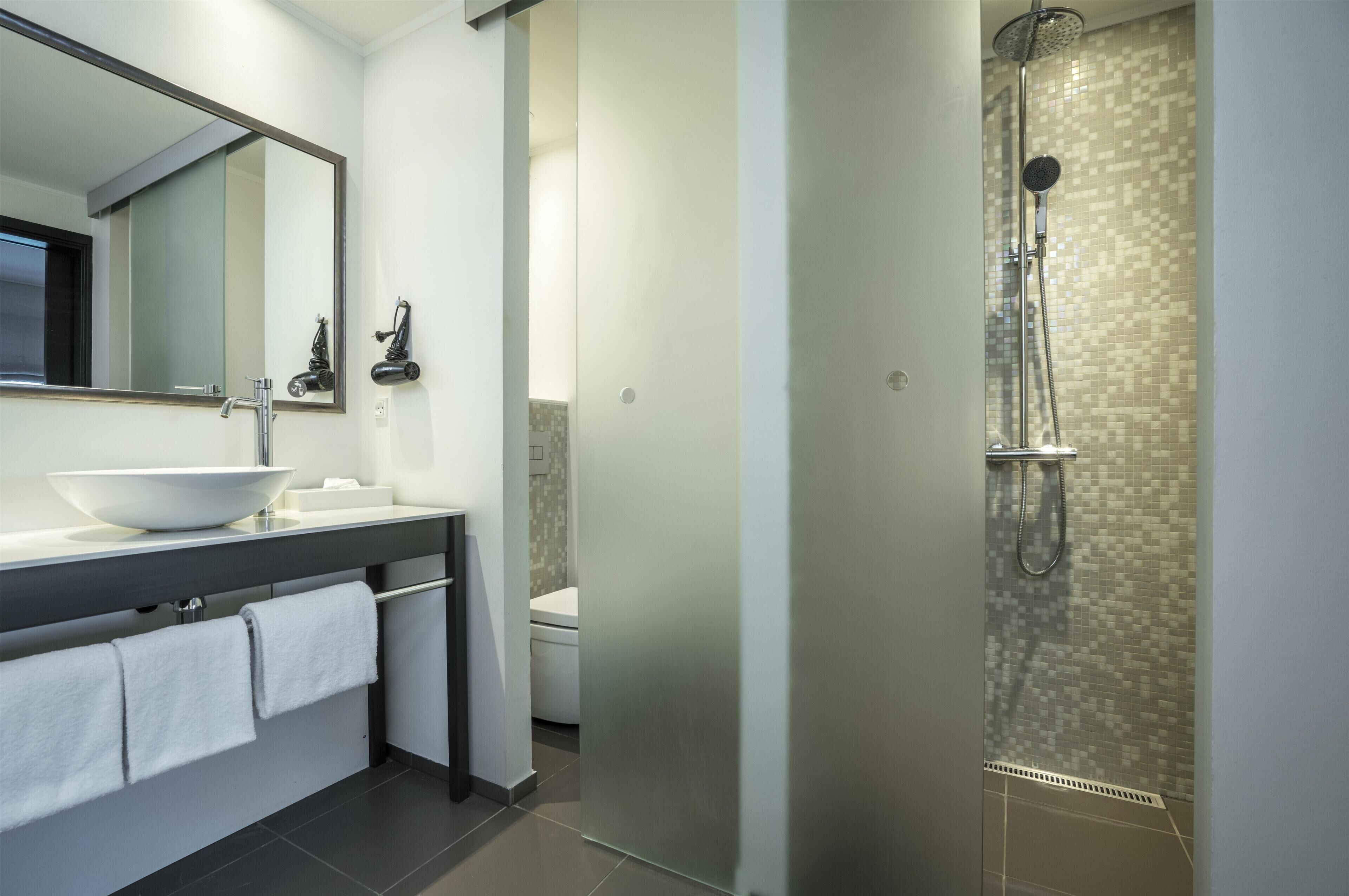 A modern bathroom with a large mirror, a sink, a toilet, and a glass-enclosed shower area.