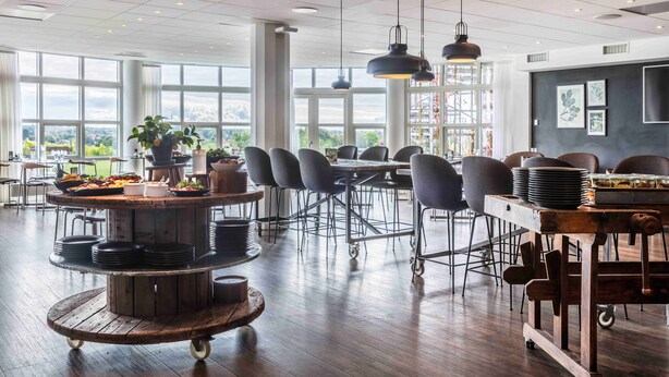 Un comedor amplio con ventanas grandes, una mesa central de madera con plataforma giratoria y sillas modernas.