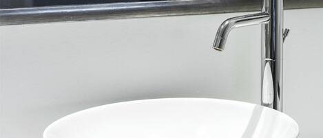 A modern bathroom with a white sink, chrome faucet, and a mirror reflecting a window.