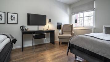 A hotel room with a bed, a desk with a chair, a television, and a window with a view of trees.