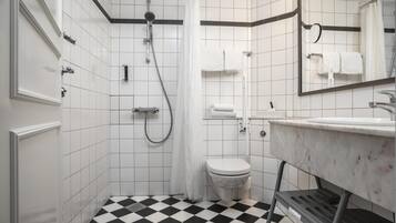 Un baño con piso a cuadros blanco y negro, inodoro blanco, ducha con cortina y lavamanos con espejo arriba.
