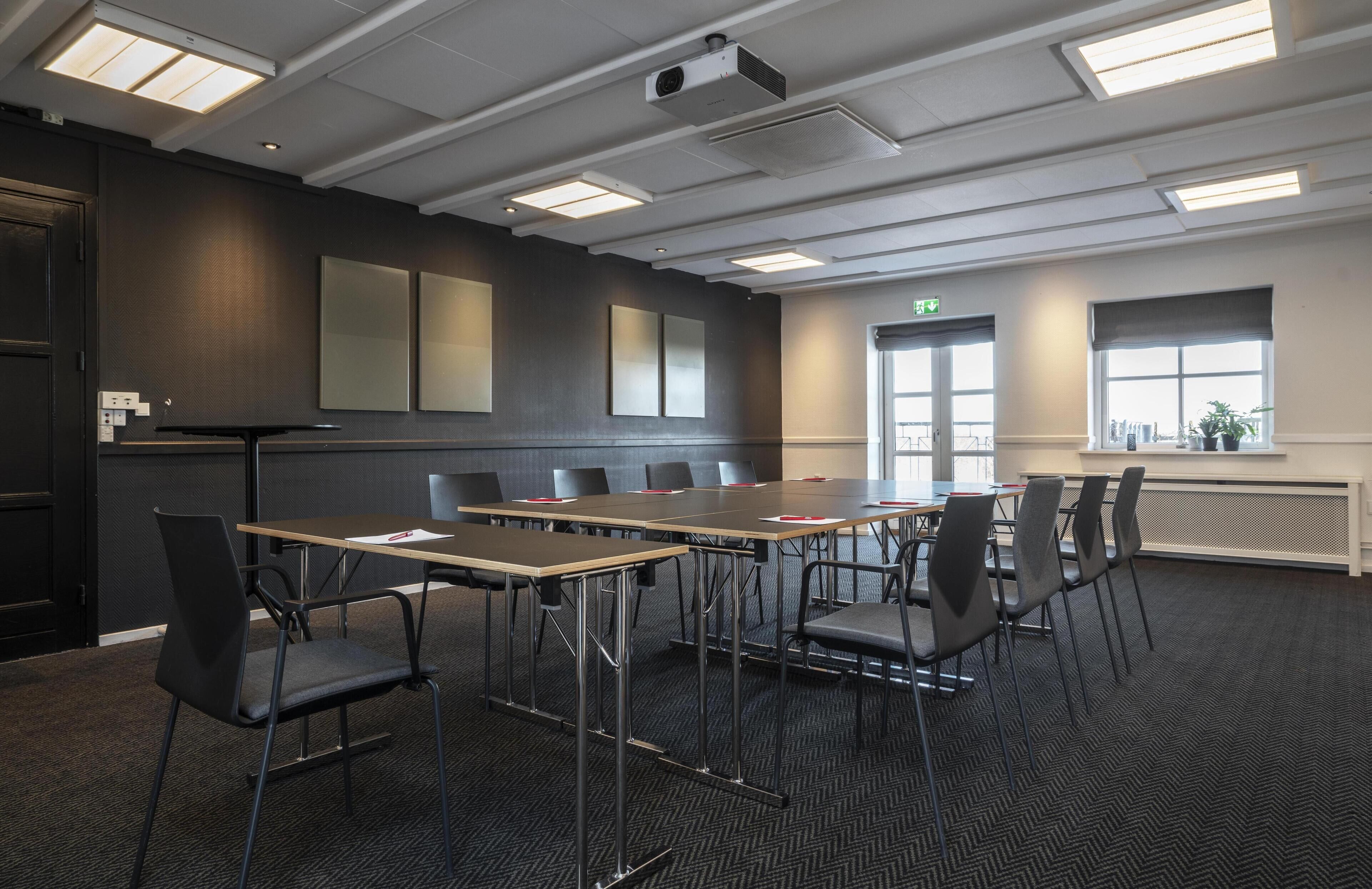 A conference room with a long table, chairs, a projector, and a window with blinds.