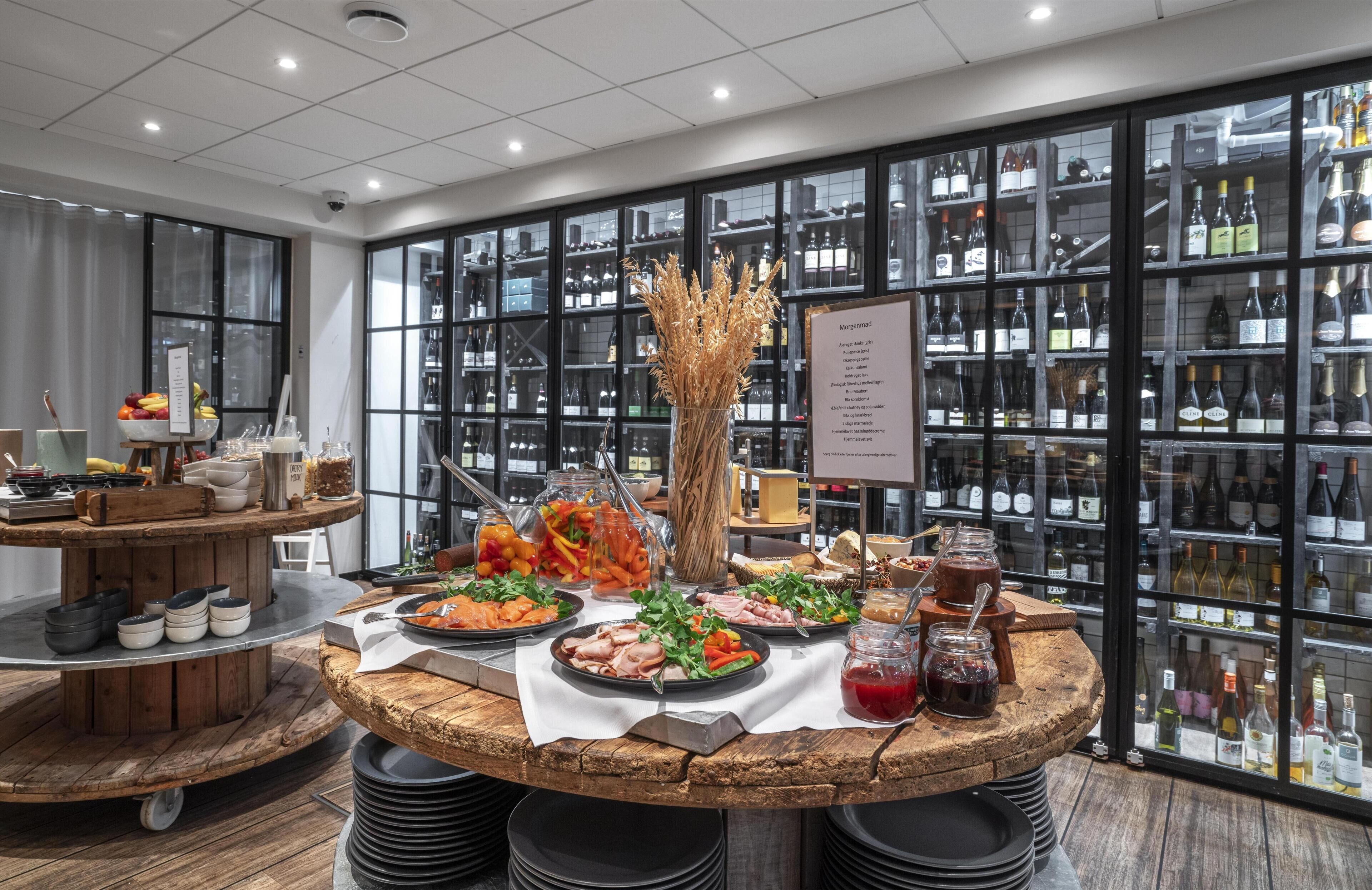 Ein Restaurant mit einem runden Holztisch, reichhaltig mit Speisen und Getränken gedeckt, umgeben von Weinflaschen in Glaskästen.