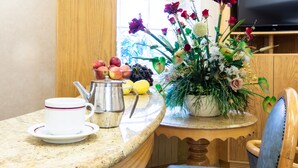 A kitchen counter with a coffee cup, teapot, fruits, and a floral arrangement. - Nayland Hotel (London)