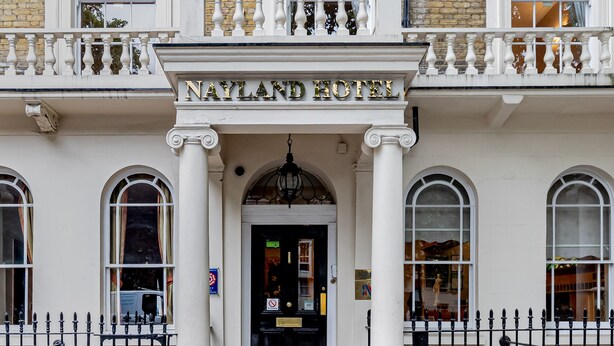 A historic building with a classic facade, featuring a prominent entrance with a black door and a balcony with white balustrades. - Nayland Hotel (London)