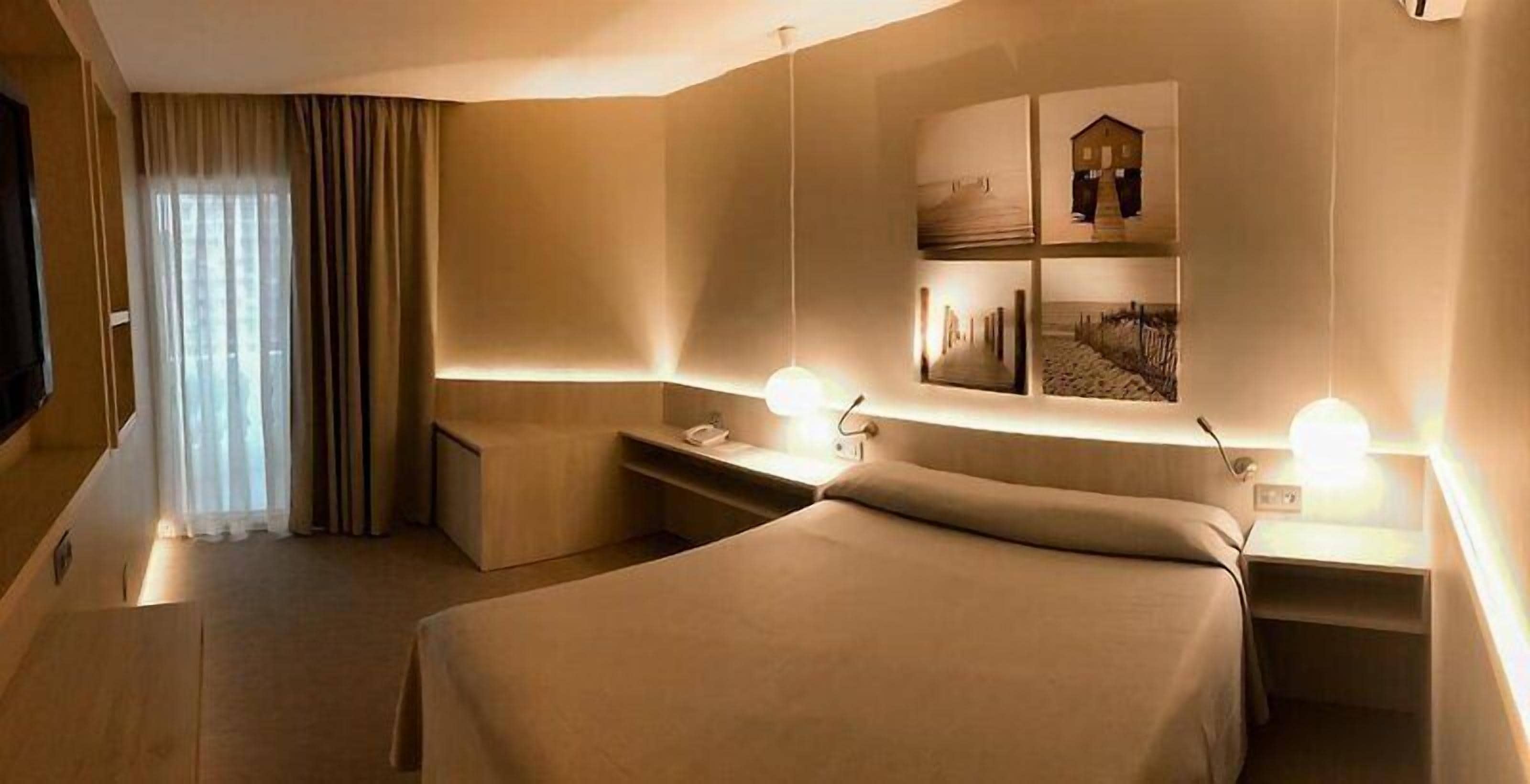 A hotel room with a bed, bedside tables, a desk, a chair, a TV, and a window with curtains.