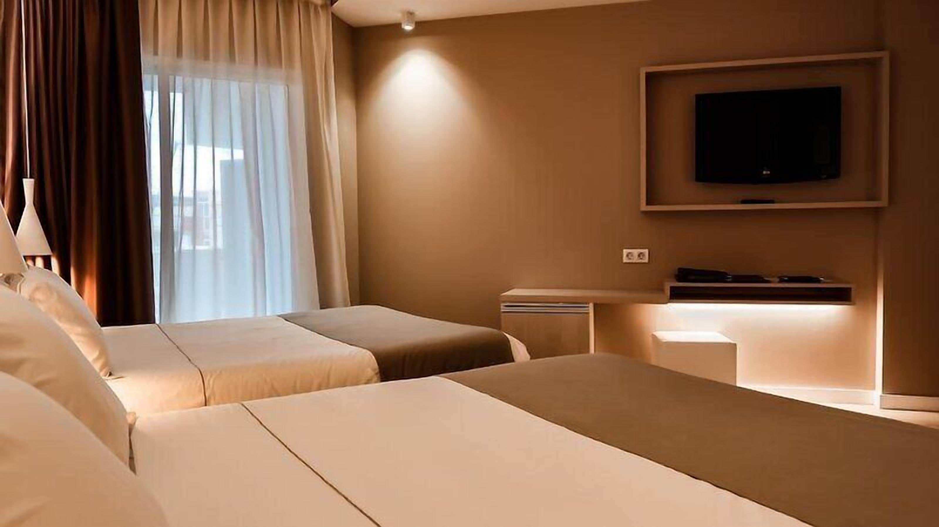 A hotel room with two beds, a TV, and a desk with a lamp.