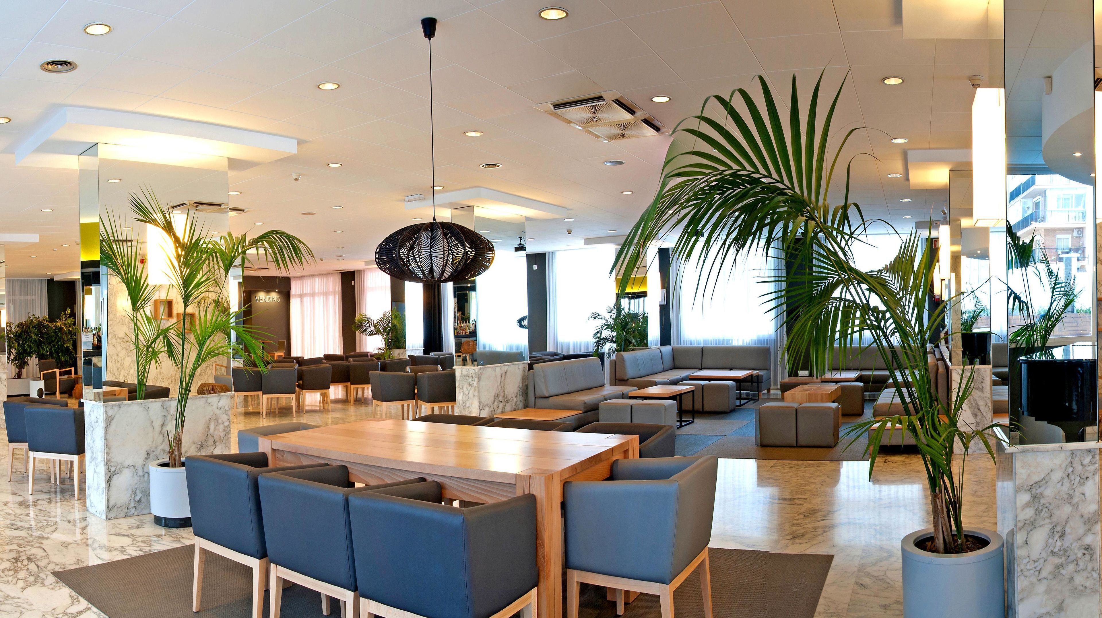 A modern hotel lobby with seating areas, a marble reception desk, and large windows.