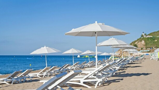 Una playa con sombrillas blancas y sillas reclinables.