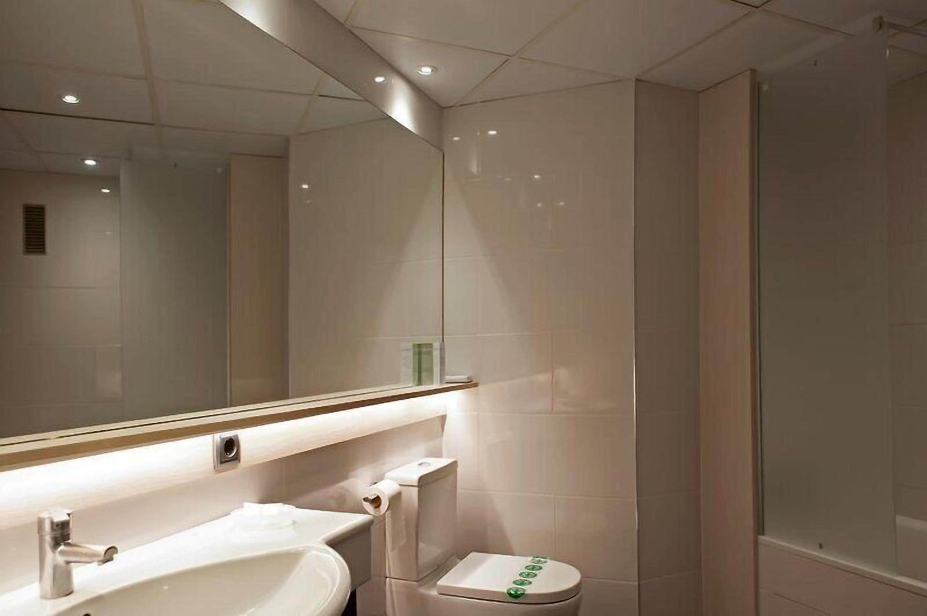 A modern bathroom with a large mirror, a sink, a toilet, and a shower area.