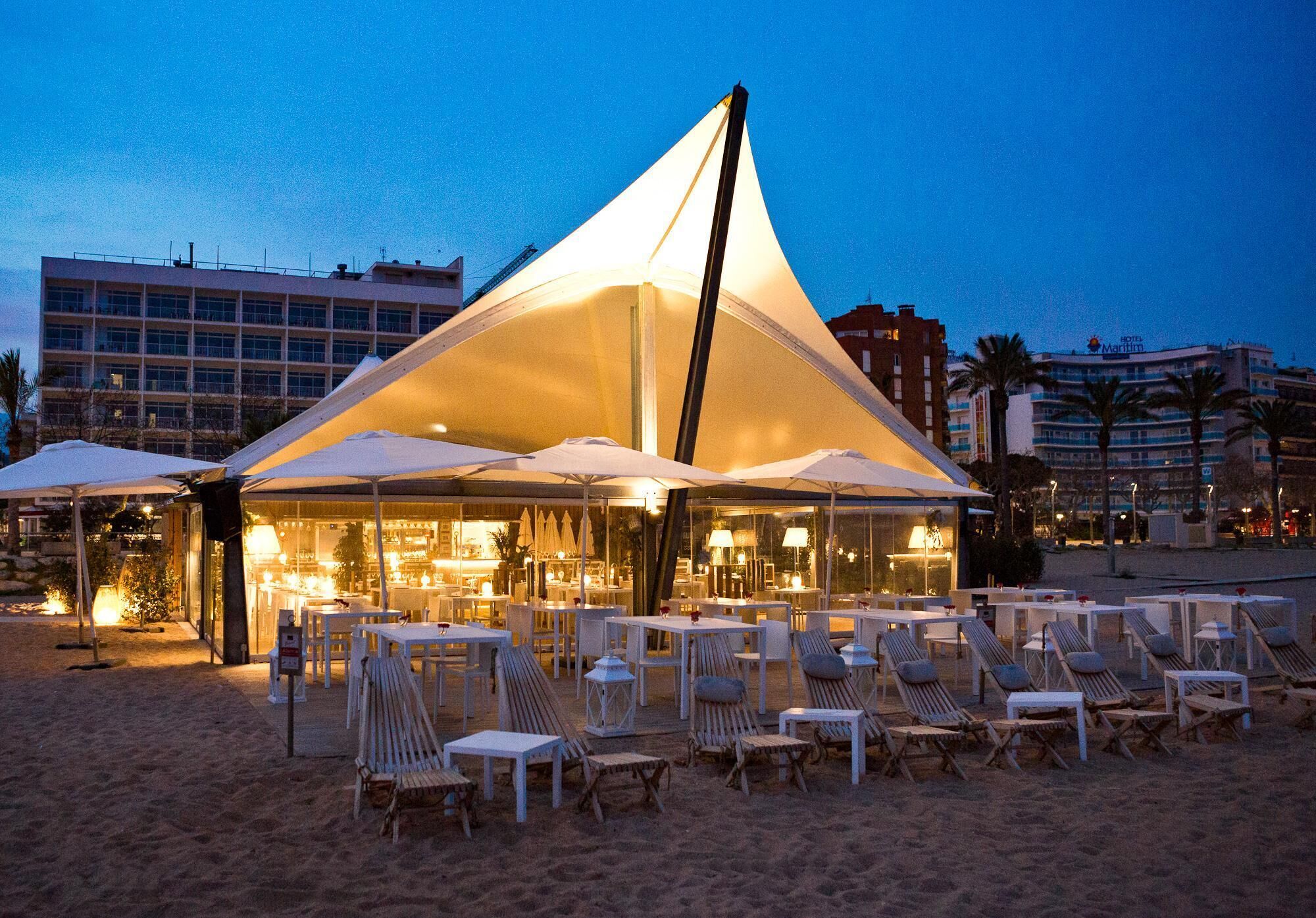 Un'area salotto all'aperto con tavoli e sedie, una grande struttura tenda e un edificio sullo sfondo.