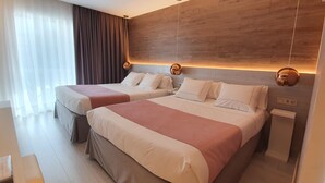 Habitación de hotel con dos camas, cabecero de madera, mesita de noche y ventana con cortinas.