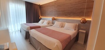 Habitación de hotel con dos camas, cabecero de madera, mesita de noche y ventana con cortinas.