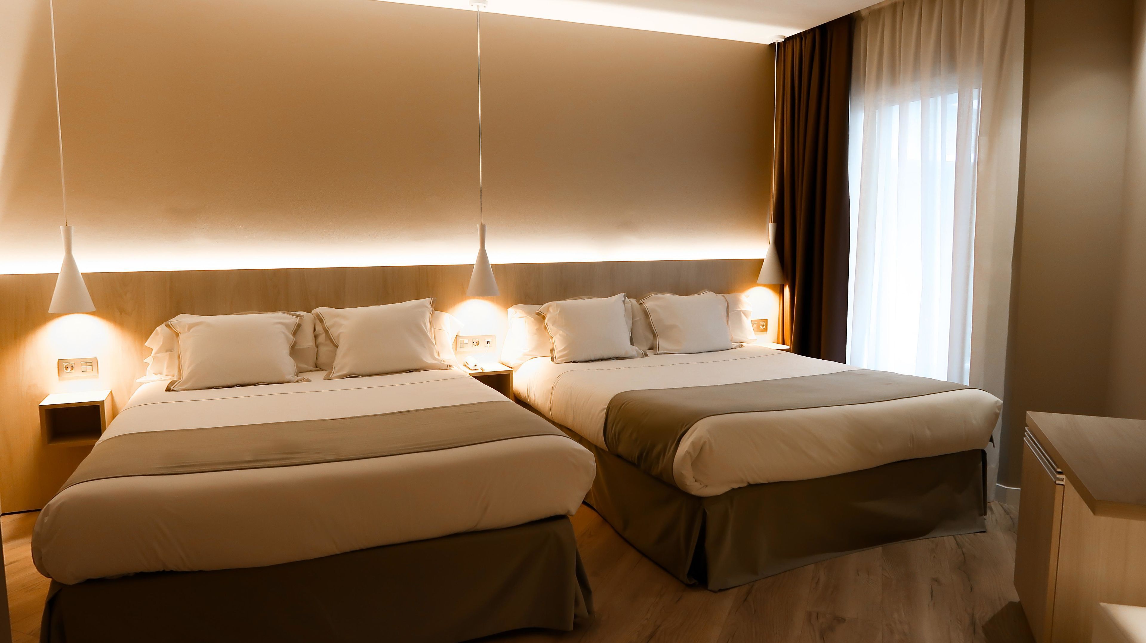 A hotel room with two beds, bedside lamps, a nightstand, and a window with curtains.