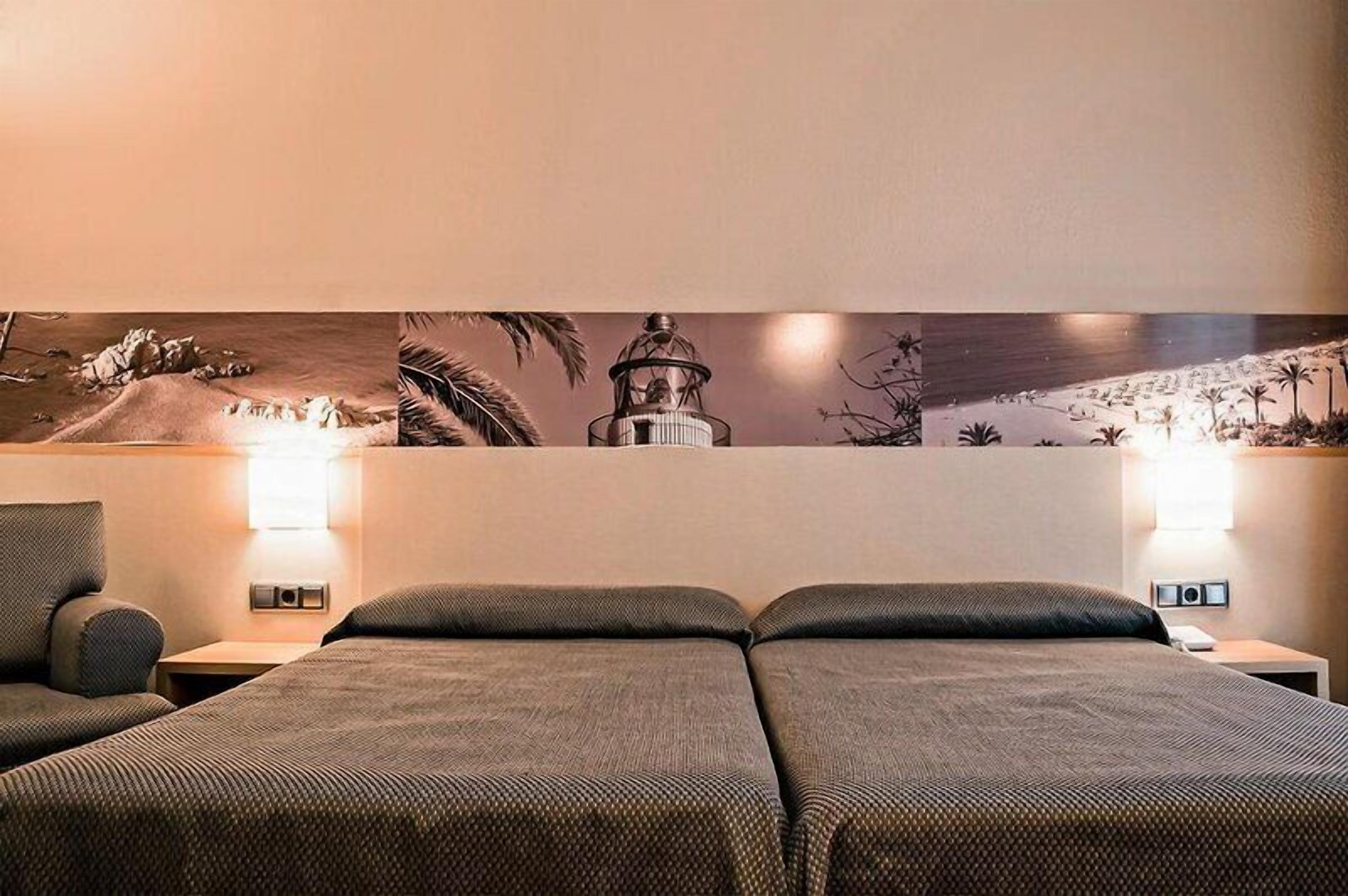 A hotel room with two beds, nightstands, wall art, and a lamp.