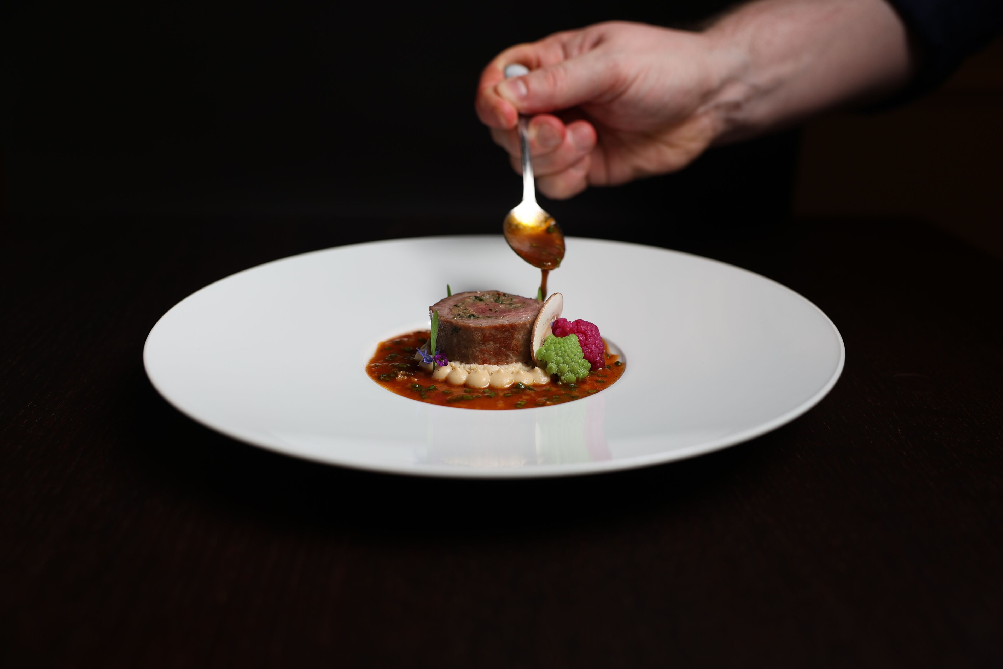 A white plate with a meat dish, garnishes, and sauce.