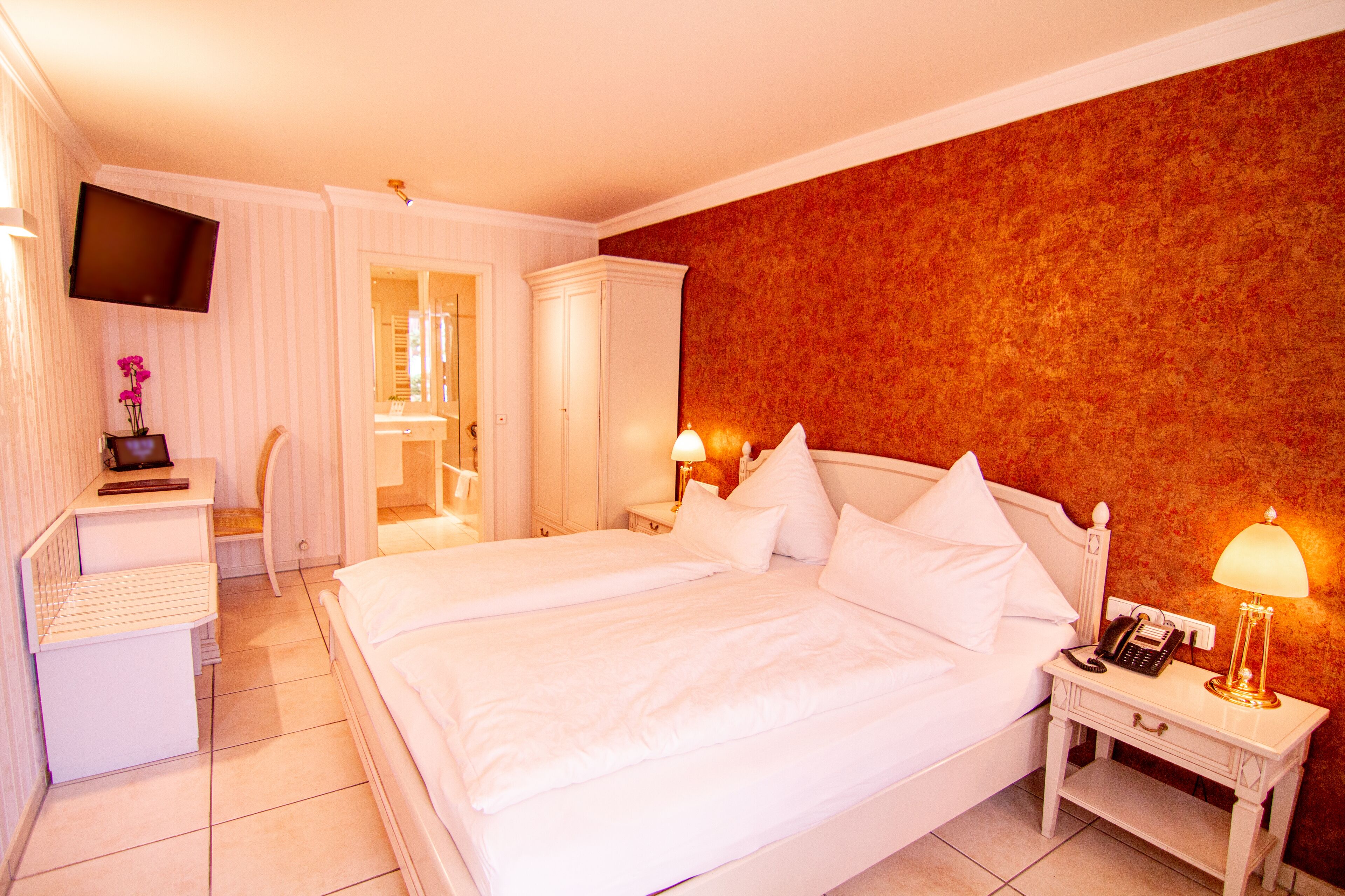 A hotel room with a large bed, bedside tables with lamps, a TV mounted on the wall, and a wardrobe.