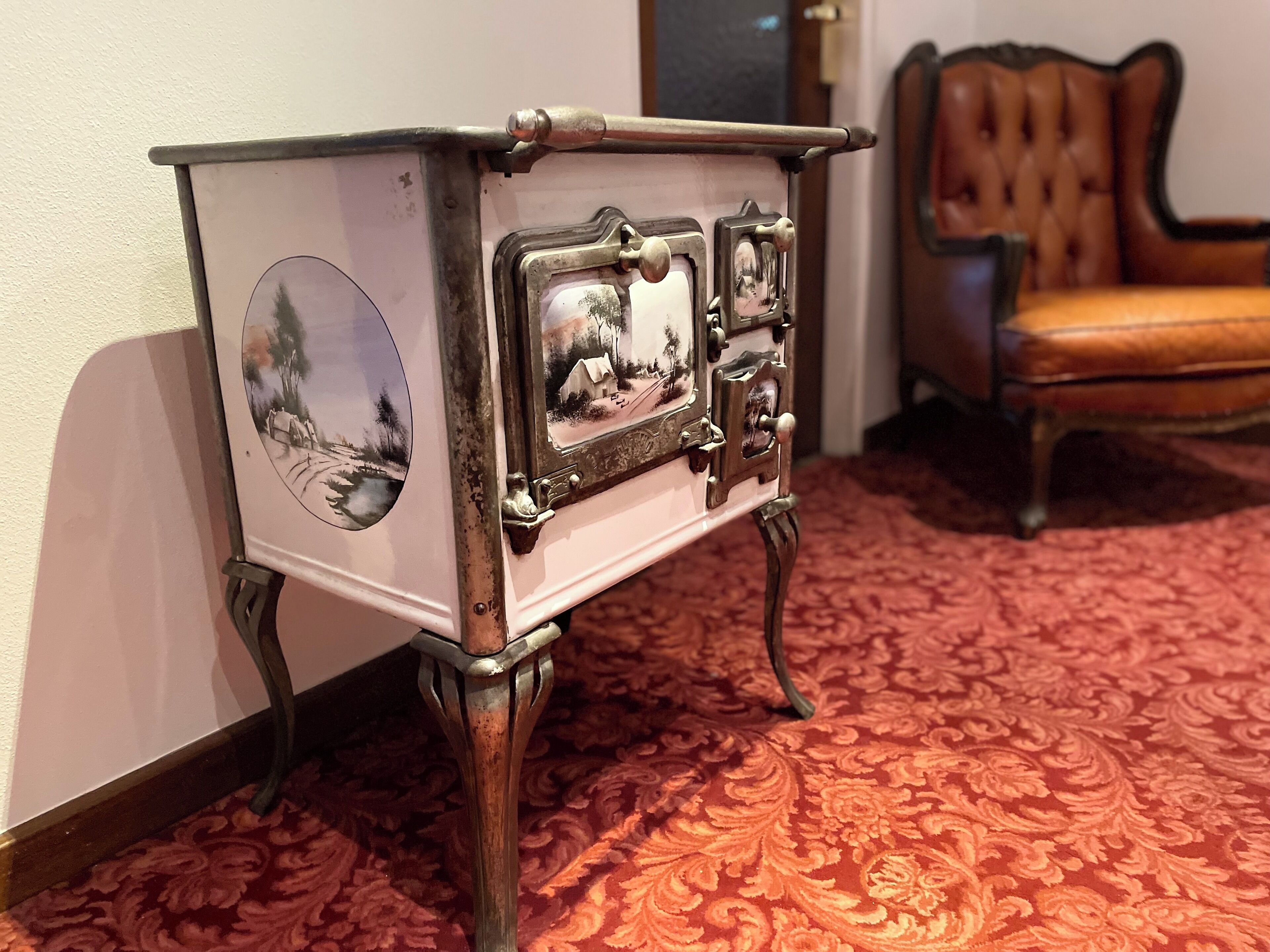Un gabinete de madera de estilo vintage con elegantes aldabillas metálicas y un panel decorativo con una escena campestre.