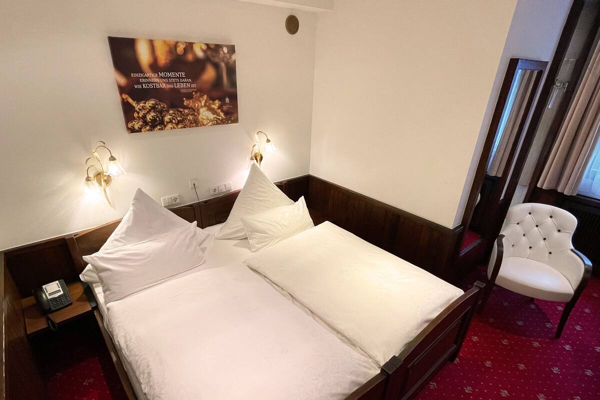 Una habitación de hotel con una cama bien hecha, una mesita de noche con un teléfono, una lámpara de pared y un cartel.