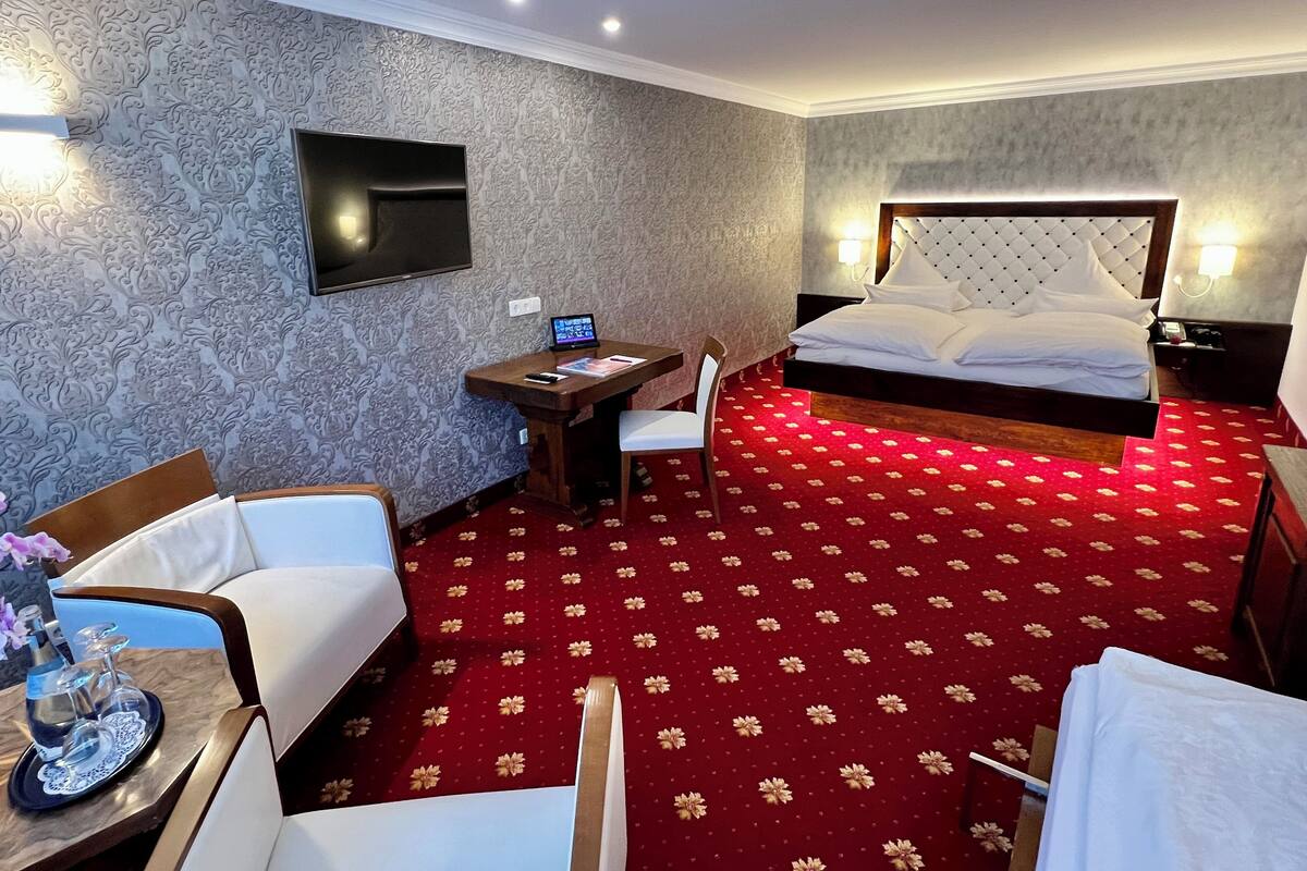 Una habitación de hotel con una cama, un escritorio con una computadora, una silla y un televisor montado en la pared.