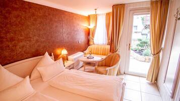 A hotel room with a bed, a small table with a lamp, a chair, and a view of the outside through a glass door.