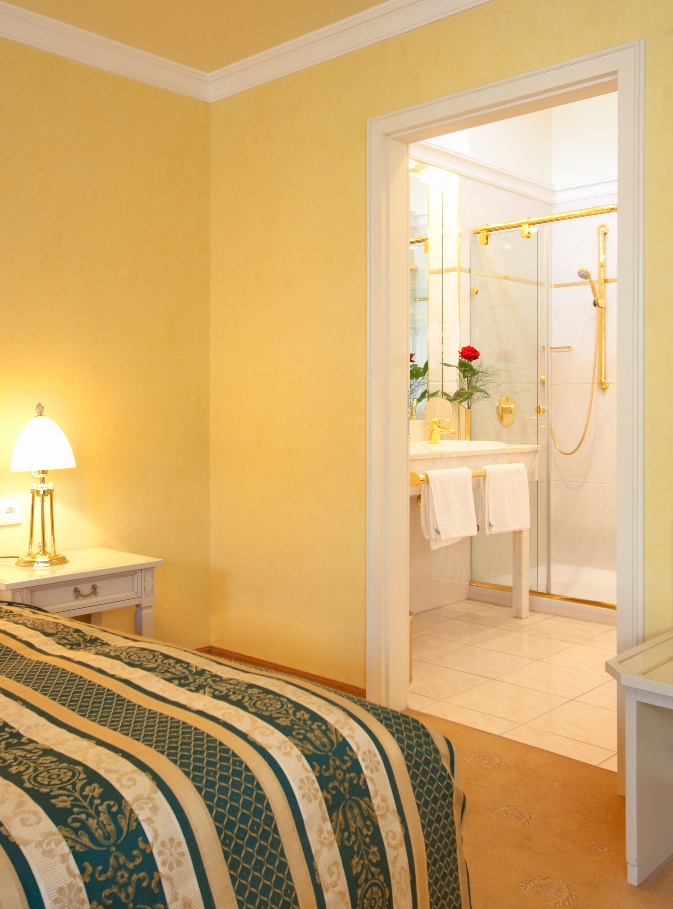 Habitación de hotel con cama, mesita de noche con lámpara, baño con ducha y espejo.