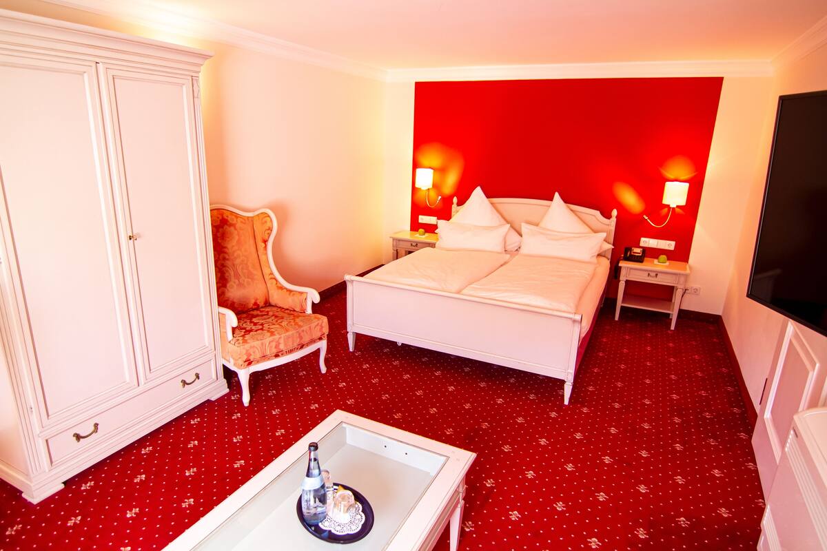 Una habitación de hotel con cama, una silla, armario, mesita de noche y televisión.