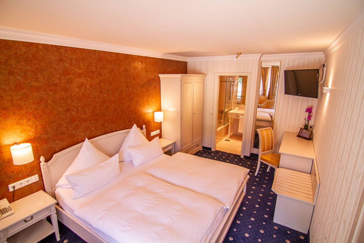 Una habitación de hotel con una cama grande, mesitas de noche, un escritorio con silla, un televisor y un espejo.