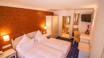 A hotel room with a large bed, bedside tables, a desk with a chair, a TV, and a mirror.