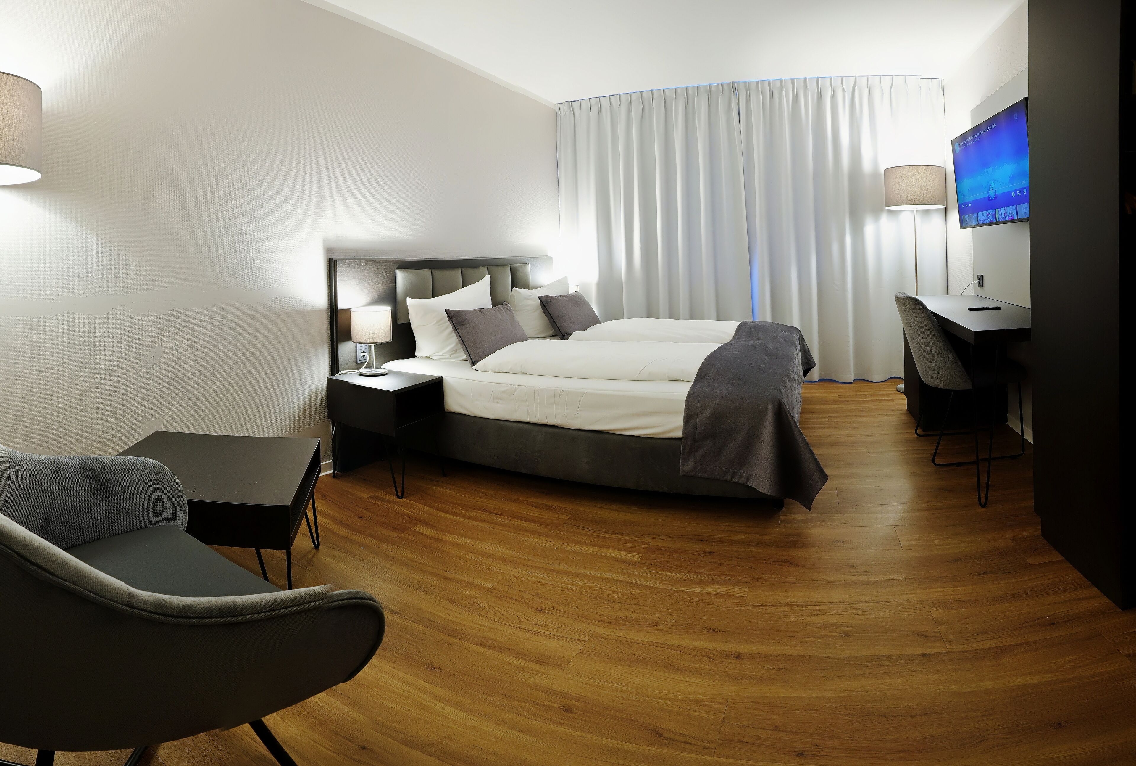 A modern hotel room with a large bed, a desk, a chair, and a TV.
