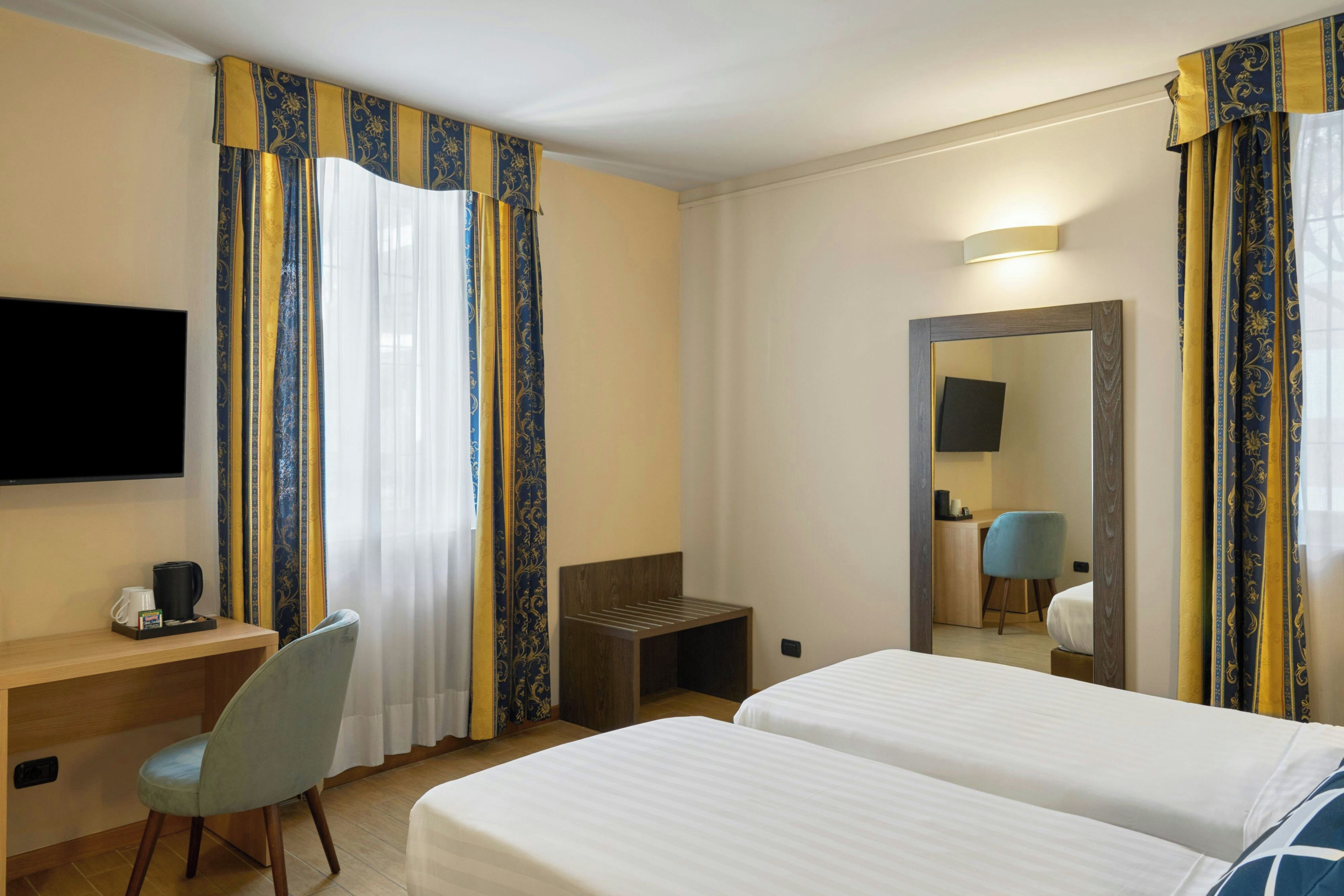 A hotel room with two beds, a desk, a chair, a coffee maker, and a television.