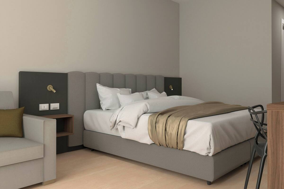 A modern bedroom with a grey bed, white bedding, a wooden nightstand, a grey armchair, and a wooden dresser.