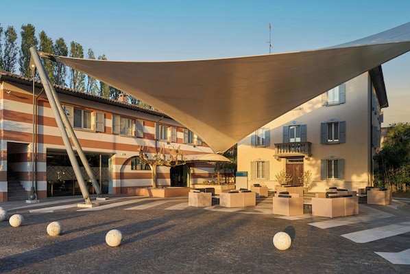 Un hotel con fachada a rayas, asientos al aire libre y una gran vela de sombra.