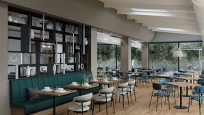 Una cafetería moderna con un sofá verde, mesas y sillas de madera, y una pared decorativa con diversos objetos.