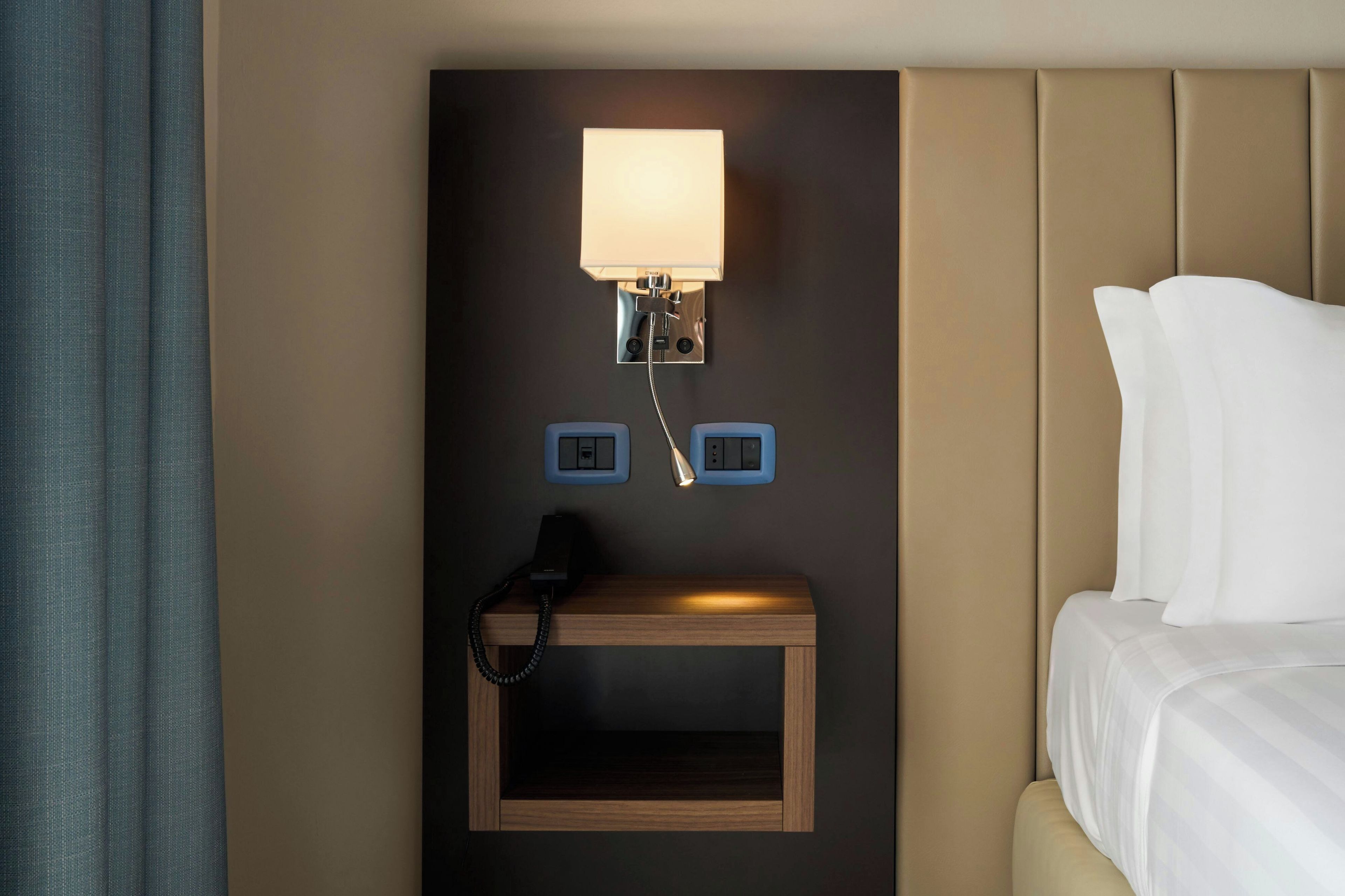 Una habitación de hotel con cama, mesita de noche, lámpara y teléfono.