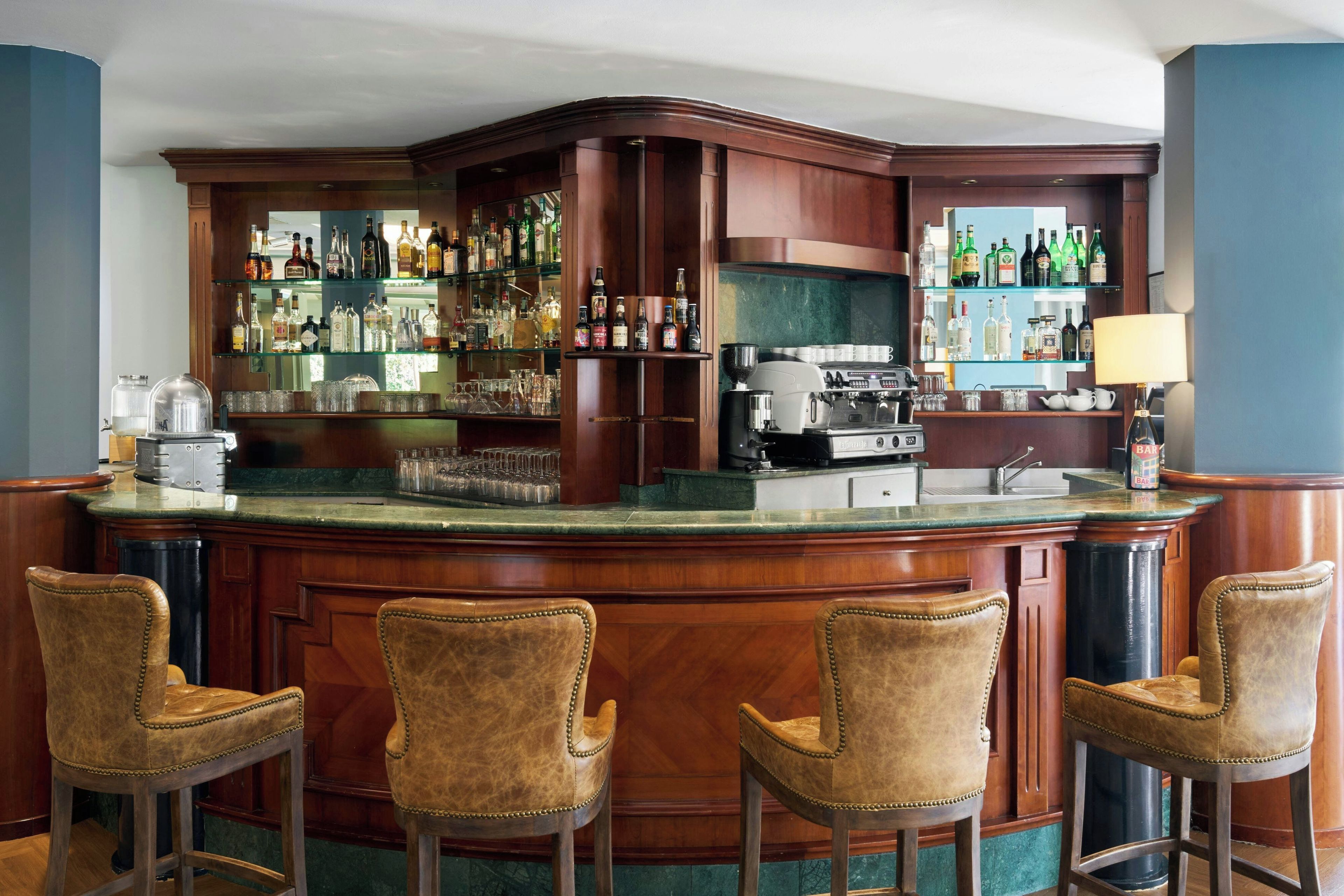 Zona de bar con mostrador de madera, taburetes y estantes llenos de botellas.