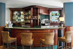 A bar area with a wooden counter, bar stools, and shelves stocked with bottles. - Four Points Flex by Sheraton Parma (Parma)